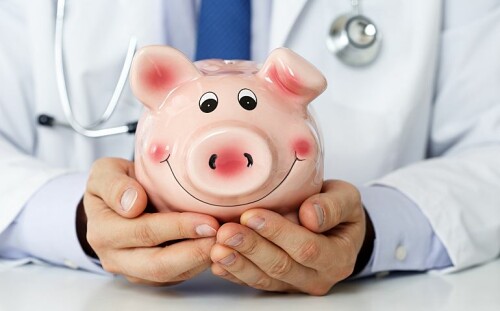 Male medicine doctor wearing blue tie holding and covering happy funny smiling piggybank in hands closeup. Medical service economy health care savings and insurance concept. Focus on piggy bank