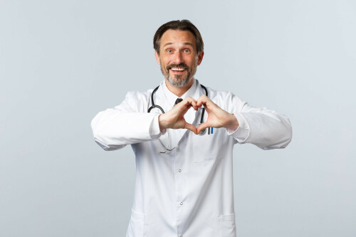 Covid-19, coronavirus outbreak, healthcare workers and pandemic concept. Happy caring male doctor in white coat, showing heart sign and smiling, express sympathy and admiration.